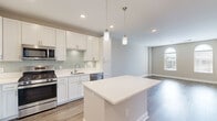 This single-floor residence showcases a thoughtfully designed open-concept layout, where the kitchen serves as a central highlight. Crisp white shaker cabinetry lines the walls, complemented by a soft green subway tile backsplash and white quartz countertops. A full suite of stainless steel appliances—including a gas range, built-in microwave, French door refrigerator, and dishwasher—adds a polished, functional edge. A central kitchen island provides additional prep space and flows naturally into the adjoining living area, which features warm wood-look plank flooring and recessed lighting throughout. Pendant lights over the island add a refined finishing touch. The bedrooms are well-proportioned, featuring plush carpeting or hardwood-style flooring and distinctive arched windows that invite generous natural light and outdoor views. Neutral warm-beige walls create a calm, versatile backdrop throughout. The bathroom is cleanly finished with a white vanity, quartz countertop, subway-tiled tub-shower combination, and wood-look flooring, offering a cohesive and contemporary aesthetic that carries through the entire space.