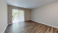 Located at Crowell Square Court in Asheville, NC, this one-bedroom, one-bathroom unit offers a well-organized, single-floor layout designed for comfortable everyday living. The open living area is finished with durable hardwood-style flooring and neutral taupe walls, creating a clean and inviting atmosphere. A large sliding glass door fitted with vertical blinds fills the living room with natural light while providing views of surrounding greenery. The kitchen is efficiently laid out in a galley style, featuring warm oak cabinetry, generous counter space with laminate surfaces, a double-basin sink, and white appliances including a range and refrigerator. A peninsula with an overhead cabinet connects the kitchen to the entryway, offering a convenient pass-through and additional storage. The bedroom is a comfortable, well-proportioned room with its own window overlooking trees, a ceiling fan with light fixture, and the same rich hardwood-style flooring found throughout. The bathroom includes tile flooring, a wooden vanity, and accessibility-friendly grab bars. An adjacent closet is outfitted with built-in wire shelving for organized storage. A textured ceiling adds a classic finishing touch throughout the unit.