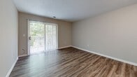 Located at Crowell Square Court in Asheville, NC, this one-bedroom, one-bathroom unit offers a well-organized, single-floor layout designed for comfortable everyday living. The open living area is finished with durable hardwood-style flooring and neutral taupe walls, creating a clean and inviting atmosphere. A large sliding glass door fitted with vertical blinds fills the living room with natural light while providing views of surrounding greenery. The kitchen is efficiently laid out in a galley style, featuring warm oak cabinetry, generous counter space with laminate surfaces, a double-basin sink, and white appliances including a range and refrigerator. A peninsula with an overhead cabinet connects the kitchen to the entryway, offering a convenient pass-through and additional storage. The bedroom is a comfortable, well-proportioned room with its own window overlooking trees, a ceiling fan with light fixture, and the same rich hardwood-style flooring found throughout. The bathroom includes tile flooring, a wooden vanity, and accessibility-friendly grab bars. An adjacent closet is outfitted with built-in wire shelving for organized storage. A textured ceiling adds a classic finishing touch throughout the unit.