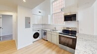 Located at 710-712 Main St in Middletown, CT, this two-story residence offers a thoughtfully designed layout spread across two floors. The main level is the larger of the two, housing an open kitchen outfitted with stainless steel appliances — including a bottom-freezer refrigerator, range, microwave, and dishwasher — complemented by white shaker cabinetry, granite countertops, classic subway tile backsplash, and light hardwood flooring. An in-unit washer is conveniently integrated into the kitchen space. A striking arched window floods the main floor with natural light, adding architectural character. Two hallways connect the living areas, and a distinctive spiral staircase leads to the upper level. The second floor hosts the carpeted bedroom, featuring a tall window with views of the surrounding brick streetscape. The cozy, well-defined bedroom space is finished with recessed lighting and clean white walls. Both bathrooms are elegantly appointed with marble-look tile flooring and walls. The full bath includes a soaking tub with a marble-surround, gold-toned fixtures, and a vanity with sink. The second bath is a clean, compact powder room with tile flooring. Throughout, the space maintains a bright, modern aesthetic with crisp white walls and quality finishes.