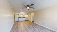 This efficient single-floor, one-bedroom, one-bathroom unit offers a well-organized layout that maximizes every square foot of its compact footprint. Throughout the space, light wood-style laminate flooring and warm neutral-toned walls create a clean, cohesive aesthetic.

The open living area serves as the heart of the unit, featuring a ceiling fan with integrated lighting and a window that allows natural light to fill the room. A wall-mounted HVAC unit provides climate control, and crown molding adds a subtle architectural detail along the ceiling's textured finish.

Directly adjoining the living area, the kitchen is efficiently designed with white shaker-style cabinetry extending to the ceiling for ample storage. Dark countertops provide contrast against the white surfaces, and the kitchen includes a full suite of white appliances — refrigerator, electric range, and a built-in range hood — alongside a single-basin sink.

The bedroom offers a comfortable and private retreat, with its own ceiling fan, a window with blinds for natural light and privacy, and a wall vent for climate control.

The bathroom is straightforward and functional, featuring a white vanity with storage, a toilet, and a full shower-tub combination, all finished in a clean, bright palette with wood-style flooring continuing from the rest of the unit.