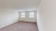 Located at 101 W Baltimore Pike in Lansdowne, PA, this one-bedroom, one-bathroom unit offers a practical and well-organized single-floor layout. The living room is generously sized, featuring neutral carpet flooring, cream-toned walls, and dual windows that bring in natural light while offering views of the surrounding neighborhood. Baseboard heating runs throughout the carpeted areas, ensuring consistent warmth. The kitchen is efficiently designed with warm wood-toned cabinetry, dark countertops, a double sink, and wood-look vinyl flooring. White appliances, including a refrigerator and electric range, are included. Adjacent to the kitchen, the dining area provides a defined space for meals. The bedroom is a comfortable size, featuring two side-by-side closets, multiple windows for natural light, and the same soft carpet found throughout the living areas. Additional closets are accessible via the hallway, offering ample storage. The bathroom is clean and functional, with a white vanity with cabinet storage, a medicine cabinet mirror with overhead lighting, and tile flooring. Overall, the unit presents a bright, neutral palette with a straightforward layout suited for everyday living.