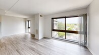 Located in Medford, MA, this 2-bedroom, 1-bathroom unit offers a well-organized single-floor layout designed for comfortable everyday living. Light gray wood-look flooring runs consistently throughout, lending a clean, cohesive aesthetic to every room.

The combined kitchen and living area forms the heart of the unit. The kitchen is outfitted with white shaker-style cabinetry, a marble-look quartz peninsula with an undermount sink, stainless steel appliances including a refrigerator, range, and microwave, and a white tile backsplash. The adjoining living area benefits from large, floor-to-ceiling windows framed in dark brown, filling the space with natural light and offering views of the surrounding Medford neighborhood and greenery beyond.

The primary bedroom is a generously sized room featuring a large sliding window that continues the unit's theme of natural light. The second bedroom is equally bright, with its own window and ample wall space. Both rooms are finished with the same light flooring and neutral white walls, providing a versatile backdrop.

The bathroom is cleanly appointed with white cabinetry, a full-size soaking tub and shower combination with white tile surround, a wall-mounted mirror, and matching light flooring. A hallway connects the living spaces to the bedrooms and bathroom, completing this functional and modern layout.