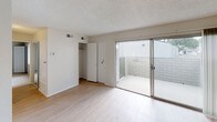 This single-floor residential unit presents a clean, functional layout across several well-defined living spaces. The main living area features light wood-style flooring and a ceiling fan, creating a bright, airy atmosphere well-suited for everyday living and relaxing. A textured popcorn ceiling runs throughout, adding a classic residential character to the space.

The kitchen is efficiently arranged with white cabinetry, a gas range, a full-size refrigerator, and granite-style countertops that extend to a dedicated workspace — providing ample room for meal preparation. The kitchen flows naturally into the rest of the unit through an open corridor layout.

A carpeted bedroom offers a quiet retreat, while a secondary room with light wood flooring includes a built-in closet and sliding glass doors that open directly onto a private enclosed patio with brick privacy walls, bringing in natural light.

The bathroom is well-appointed with a granite-style undermount sink, bright vanity lighting, a large mirror, and convenient access to additional storage areas with open shelving, ideal for organization.

Throughout the unit, neutral tones on the walls complement the light flooring, creating a cohesive and versatile palette ready for personalization. The space is thoughtfully designed to balance practicality with comfortable everyday living.