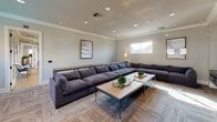 This contemporary single-floor lounge and media room is thoughtfully designed for both relaxation and entertainment. The space is anchored by a generously sized L-shaped sectional sofa upholstered in deep charcoal fabric, arranged around a rustic wood-and-metal coffee table accented with decorative greenery. Neutral-toned walls, crown molding, and recessed lighting overhead create a refined yet comfortable atmosphere, while patterned carpet flooring adds warmth and texture underfoot.

The entertainment wall is a standout feature, showcasing multiple large flat-screen televisions mounted above a sleek, dark built-in media console with ample drawer storage. This setup makes the space ideal for watching multiple broadcasts or presentations simultaneously. A bar-height communal table with metal-framed stools is positioned nearby, offering a more casual seating option perfect for gathering or working.

Natural light filters in through a series of horizontal windows positioned along the upper portion of the walls, maintaining privacy while brightening the interior. A floor lamp and framed wall art contribute to the curated, welcoming ambiance. The open layout allows for easy movement throughout the room, making it well-suited as a shared amenity or common area lounge. Overall, the space balances modern design sensibilities with functional, multi-use versatility.