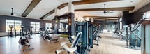 This expansive 5,060 square foot fitness center is a testament to modern gym design and functionality. The space is divided into distinct zones, each catering to different workout styles. The weight training area boasts an impressive array of free weights, weight machines, and power racks, all arranged for optimal flow and safety. A dedicated cardio section features top-of-the-line treadmills, ellipticals, and stationary bikes, positioned to take advantage of natural light from large windows.

The facility's design seamlessly blends aesthetics with practicality. Vaulted ceilings with exposed wooden beams create an airy, spacious feel, while industrial-style ceiling fans ensure proper ventilation. Stylish pendant lights add a touch of elegance, contrasting beautifully with the functional gym equipment. The flooring transitions from durable carpeting to hardwood and specialized rubber matting in different zones, enhancing safety and comfort.

A notable feature is the functional training area, complete with suspension trainers, battle ropes, and a turf strip for sled pushes. Large mirrors line the walls, allowing members to monitor their form during workouts. The thoughtful layout promotes easy navigation between different exercise stations, making the most of the generous square footage.

Overall, this fitness center combines cutting-edge equipment with intelligent design, creating an inviting and efficient space for fitness enthusiasts of all levels.