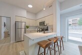 Located at 70 Dean Avenue in Barrie, Ontario, this well-appointed one-bedroom, one-bathroom unit offers a thoughtfully designed layout that maximizes every square metre of its compact footprint. The open-concept kitchen and living area forms the heart of the home, where light wood laminate flooring and crisp white walls create a clean, modern atmosphere. The kitchen is fully equipped with stainless steel appliances — including a refrigerator, electric range, built-in microwave, and dishwasher — complemented by white cabinetry, a white quartz countertop, and a functional peninsula that doubles as a breakfast bar. Natural light streams through a large window in the living area, which offers a view of the outdoors and provides a welcoming space for relaxing or entertaining. The bedroom features a mirrored sliding closet, a dedicated window with outdoor views, and elevated ceiling details that lend a sense of openness. The bathroom is finished with elegant marble-look tile flooring and a full soaker tub with an arched surround, maintaining the home's clean white aesthetic. A utility room rounds out the layout, adding practical storage functionality. Throughout the unit, the cohesive neutral palette, quality finishes, and efficient design come together to create a comfortable and stylish living environment.