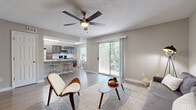 Located in Pensacola, FL, this single-floor, 2-bedroom, 2-bathroom residence offers a thoughtfully designed layout that maximizes comfort and functionality. The open-concept living area features light wood-style flooring, neutral toned walls, and a ceiling fan, creating a bright and welcoming atmosphere. A large sliding glass door floods the space with natural light and provides views of lush greenery beyond the patio. The living area flows seamlessly into the kitchen, which is outfitted with dark taupe cabinetry, marble-style quartz countertops, a subway tile backsplash, and a full suite of stainless steel appliances including a refrigerator, range, microwave, and dishwasher. A breakfast bar with seating adds casual dining convenience. Both bedrooms are carpeted for comfort and include ceiling fans and dedicated closets. The primary bedroom offers a generous footprint with ample natural light. The two bathrooms feature dark wood vanities with white countertops and a tub-shower combination. Two hallways and two closets provide practical storage throughout. The textured ceilings and consistent neutral palette tie the entire residence together with a clean, modern aesthetic.