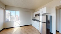 Located on the eighth floor at 515 West Sprague Avenue in the heart of downtown Spokane, Washington, Unit 817 is a well-appointed residence offering a thoughtfully designed open-concept layout with clean, modern finishes throughout. Light hardwood flooring flows seamlessly across the main living areas, complementing the bright, neutral walls and textured ceilings that define the space.

The kitchenette is efficiently designed with crisp white cabinetry, dark countertops, a stainless steel refrigerator, built-in microwave, and a single-basin sink — providing all the essentials in a compact, stylish package. A large sliding glass door and oversized windows flood the living area with natural light while framing views of the surrounding Spokane cityscape, giving the space an airy, elevated feel.

The bedroom area is spacious and open, with generous wall space and continued hardwood flooring, offering a clean canvas for a variety of layouts. The bathroom features white subway tile surrounding a full soaking tub and shower, tile flooring, and a granite-topped vanity, lending a polished and timeless aesthetic. A dedicated laundry area with a stacked washer and dryer adds a practical and desirable convenience to the unit. This residence offers comfortable urban living in a prime downtown location.