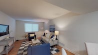 This single-floor residence offers a thoughtfully designed layout that balances comfort and functionality. The open-concept living and dining area is anchored by warm hardwood flooring, neutral-toned walls, and a seamless flow between spaces. The living room provides ample room for seating arrangements and features a window that allows natural light to brighten the interior. Adjacent to it, the dining area accommodates a glass-top table and is accented by a decorative sunburst wall mirror, adding an elegant touch to the space.

The kitchen is equipped with rich dark-wood cabinetry, granite countertops, a white tile backsplash, and a full suite of stainless steel appliances including a gas range, refrigerator, and dishwasher, complemented by recessed lighting overhead.

The primary bedroom is a serene retreat with hardwood floors, a ceiling fixture, and a window dressed with blinds for privacy. A second bedroom mirrors the same comfortable aesthetic with natural light and warm flooring.

The bathroom is finished with large-format marble-look tile flooring, a dark vanity with granite countertop, and a tub-shower combination with a marble-surround enclosure, conveying a clean and polished design throughout.