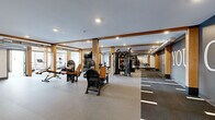 Located at 4066 Lexington Ave N in Shoreview, Minnesota, this professionally designed fitness facility spans a generously sized single floor, offering a comprehensive workout environment across multiple distinct zones. The main exercise area is defined by warm wood beam columns and recessed lighting, creating an inviting yet energetic atmosphere. It is outfitted with a wide array of strength training equipment, including multi-functional cable machines, power racks, barbells, weight plates, and an extensive dumbbell rack, all set on durable rubberized flooring. Motivational signage — including a bold "YES. YOU. CAN." mural — adorns the dark accent walls, reinforcing an encouraging training environment. Large mirrors throughout enhance spatial depth and support proper form during workouts. A dedicated cardio zone features treadmills, an elliptical, and a rowing machine, bathed in abundant natural light from floor-to-ceiling windows that offer outdoor views. A separate room serves as an indoor golf simulator space, complete with green turf flooring, a projector, and large windows that flood the area with natural light. The facility also includes additional support spaces, completing a well-rounded, amenity-rich fitness destination.