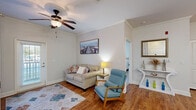 Located at 3815 Maypop Cir in Myrtle Beach, SC, this well-designed single-story, one-bedroom, one-bathroom home offers a thoughtfully utilized layout with a warm coastal aesthetic throughout. Warm hardwood flooring and crown molding flow through the main living areas, lending a polished, cohesive character to the space. The living room is bright and welcoming, featuring a ceiling fan, a glass-paneled exterior door that invites natural light, and a cozy arrangement ideal for relaxing. Adjacent to the living room, a stylish entry area includes a decorative console table, a framed mirror, and wainscoting detail that continues into the dining nook. The dining area accommodates intimate gatherings with a round wood table and tufted seating beneath warm-toned wall art. The kitchen is efficiently appointed with rich, medium-toned cabinetry, a full suite of appliances, and a generous light-colored countertop peninsula with bar stool seating — ideal for casual dining or meal prep. The spacious bedroom offers plush carpeting, dual windows with natural light, a ceiling fan, and a serene, restful ambiance. The bathroom features hardwood-style flooring, a tub-shower combination with white tile surround, and a granite-topped vanity. This home combines functional design with coastal charm in a convenient Myrtle Beach location.