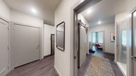 This single-floor residence offers a thoughtfully designed layout that blends modern aesthetics with functional living. The living area serves as the heart of the space, featuring dark hardwood-style flooring, neutral walls, and a ceiling fan overhead. Large windows dressed with teal curtains and horizontal blinds flood the room with natural light, creating a bright and welcoming atmosphere. The open layout connects the living area seamlessly to the kitchen, which is equipped with stainless steel appliances, including an electric range and over-the-range microwave, complemented by granite countertops, white cabinetry, and a subtle tile backsplash.

The hallway connects the main living spaces to the private areas of the unit and features a full-length mirror, recessed lighting, and a stylish sliding barn door that opens into the bedroom. The bedroom is generously sized, benefiting from multiple windows with teal drapery that allow ample natural light. A ceiling fan adds comfort overhead.

The bathroom is accessible through the bedroom and includes a glass-enclosed walk-in shower with tile surround, a vanity with granite counters, and direct access to a walk-in closet with built-in shelving and hanging rods. Throughout, the consistent use of dark hardwood-style flooring and clean white walls creates a cohesive, contemporary feel.