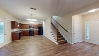 This two-story home offers a practical and comfortable layout spread across two well-appointed floors. The main level features an open-concept living and dining area finished with durable hardwood-style flooring that runs throughout. A ceiling fan anchors the living room, which is bathed in natural light from multiple windows and a rear glass door. The kitchen is outfitted with rich wood cabinetry, dark granite-style countertops, a double sink, and black appliances including a range, refrigerator, and dishwasher. Pendant lighting adds a finishing touch over the kitchen workspace. A convenient half bath on the main floor includes a pedestal sink, oval mirror, and wood-style flooring. A carpeted staircase with a classic wooden banister leads to the upper level, where the bedrooms are located. Each bedroom features plush carpet, a ceiling fan with light, natural light from windows, and generous closet space. The primary suite includes a spacious walk-in closet with wire shelving systems. The upper-level full bathroom is equipped with a single vanity, large mirror, and a tub/shower combo. A dedicated laundry area with a full-size washer and dryer completes this well-organized home.