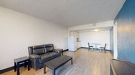This efficiently designed 1-bedroom, 2-bathroom unit makes excellent use of its single-floor layout. Light wood-style flooring runs consistently throughout, lending a cohesive and clean look to the entire space. The open-concept living area flows directly into the compact kitchen, creating an airy and functional common space. The living room features a textured ceiling, a wall-unit air conditioner, and a sliding glass door that brings in natural light and provides outdoor access. The kitchen is neatly appointed with light wood cabinetry, a built-in microwave, an electric cooktop, a single-basin sink, and a full-size refrigerator — offering all the essentials in a streamlined design. The spacious primary bedroom is a standout feature, highlighted by a bold blue accent wall that adds a striking visual element. It includes a large window with vertical blinds for natural light control and a dedicated closet with wire shelving for storage. The two bathrooms provide practical convenience, with one featuring a full tub-shower combination with grab bar accessibility. Throughout the unit, the textured ceilings, light-toned walls, and consistent flooring create a straightforward, functional living environment suited for efficient, everyday living.