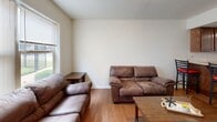 Located at 671 Washington St in Indiana, Pennsylvania, this two-floor residence offers a practical and well-organized layout suited for comfortable everyday living. The living area features warm hardwood-style flooring and is furnished with ample seating, with natural light streaming in through a window overlooking the exterior. The kitchen is well-equipped with warm wood cabinetry, generous counter space, a double sink, and full appliances including an electric range, over-the-range microwave, and a stainless steel refrigerator, all beneath a drop ceiling. Multiple carpeted bedrooms are spread across both floors, each featuring neutral walls, blinds-fitted windows that allow for natural light, and sufficient space for a bed and study area. The bathrooms are cleanly finished, one featuring warm-toned tile flooring, a wood-trimmed vanity with a large mirror, and standard fixtures, while another offers a textured wall finish and a well-appointed vanity. Throughout the residence, a consistent neutral color palette and clean finishes contribute to a calm, functional ambiance. The multi-floor layout provides a logical separation of living and sleeping spaces, making this a well-structured home in a convenient Indiana, PA location.