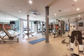 Located in Atlanta, GA (30316), this fitness center is a thoughtfully designed, single-floor facility built to support a full range of workout routines. The space features durable speckled rubberized flooring throughout, providing both safety and comfort during exercise. Recessed lighting illuminates the entire area evenly, while large windows along one wall invite generous natural light and offer views of the surrounding greenery, creating an open and energizing atmosphere.

The facility is divided into distinct functional zones. A free weights area houses a full rack of dumbbells alongside adjustable benches, including a Hoist adjustable bench, and a multi-function power rack, catering to a variety of strength training exercises. A dedicated strength machines section features multiple Fitcо cable and weight-stack machines, including cable crossover stations, seated press machines, and leg equipment, positioned against floor-to-ceiling mirrors that amplify the sense of space.

A bold orange accent wall anchors the conditioning zone, which includes medicine balls, stability balls, and additional resistance machines. A wall-mounted flat-screen television provides entertainment during workouts. Near the entrance, two water fountains and a waste station offer convenient hydration and hygiene amenities. The overall design is clean, functional, and well-maintained, delivering a complete fitness environment.