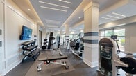 Located at 2200 Aureum Drive in Franklin, TN, this fitness center spans a generous single-floor layout divided into two distinct exercise rooms, offering a comprehensive and well-appointed workout environment. The space features a modern, clean aesthetic with white walls, coffered and tray ceilings with linear LED lighting, recessed fixtures, and rubber-floored surfaces throughout.

The primary exercise room is expansive and dedicated to strength and cardio training. It houses a full lineup of Bodycraft treadmills and ellipticals positioned along large picture windows that flood the space with natural light and provide views of the surrounding exterior. A robust strength training section includes multi-station cable machines, a barbell rack with weight plates, a full rack of dumbbells, and adjustable benches — all supported by wall-mounted mirrors that visually expand the room. Flat-screen TVs are mounted for entertainment during workouts.

The secondary exercise room offers a more versatile studio-style setting. It features stationary Expresso bikes with interactive screens, a kettlebell rack, stability and medicine balls, step platforms, a punching bag, and a wall-mounted television. A ceiling fan, large windows overlooking the exterior, and decorative moss wall accents contribute to an inviting and energizing atmosphere. A mirrored barre wall adds further functionality to the studio space.