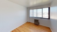 Seaway Terrace presents a well-maintained 2-bedroom, 1-bathroom single-floor residence designed with simplicity and functionality in mind. Throughout the living areas and bedrooms, warm honey-toned hardwood floors create a cohesive and inviting atmosphere, complemented by crisp white walls that keep the space feeling bright and open.

Both bedrooms are generously proportioned, each featuring large windows dressed with vertical blinds that allow for adjustable natural light and views of the surrounding neighborhood. Wall-mounted heater units are present in the bedrooms, providing direct climate control. The rooms offer a clean, neutral canvas well-suited for a variety of furnishing styles.

The kitchen is thoughtfully laid out with ample white cabinetry extending to the upper walls for storage, light-toned laminate countertops that wrap around in an L-shape, a stainless steel sink, and a gas range — providing all the essentials for efficient meal preparation.

The bathroom is neatly appointed with tile flooring, a wooden vanity with storage, an overhead vanity light with mirror, a towel bar, and a bathtub with a shower, offering a complete and functional design.

The overall floor plan, as seen in the dollhouse view, reflects an efficient single-level layout with a clear separation between the living, kitchen, and sleeping areas, making this a practical and comfortable residence at Seaway Terrace.