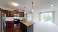 This single-floor residence offers a thoughtfully designed open-concept layout that seamlessly connects the kitchen and living areas. The kitchen is a standout feature, showcasing rich dark cherry wood cabinetry that extends to the ceiling, stainless steel appliances including a refrigerator, microwave, and range, and a curved center island topped with golden granite countertops and an undermount double sink. Pendant lighting above the island adds a refined touch, while hardwood flooring grounds the space with warmth.

The living area transitions to plush neutral carpet and is anchored by a tile-surround fireplace. Floor-to-ceiling sliding glass doors open to a private balcony with outdoor views of mature greenery, filling the room with natural light. The bedrooms are carpeted and finished in soft neutral tones, with windows offering pleasant outdoor views.

The primary bathroom features rich cherry cabinetry, a long vanity with white countertops, and direct access to a walk-in closet with built-in shelving. A secondary bathroom offers dark cabinetry, a tall storage tower, and earthy tile flooring. A dedicated laundry room with side-by-side washer and dryer and overhead cabinetry completes this well-equipped residence.