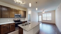 This single-story unit located at Sara Jane Parkway in Grand Prairie, Texas, presents a well-designed open-concept layout that connects the kitchen and living areas seamlessly. The kitchen is a standout feature, showcasing rich dark-wood cabinetry, granite countertops, a tile backsplash, and a full suite of stainless steel appliances including a refrigerator, range, and built-in microwave. A central island with a double sink and pendant lighting above adds both functionality and style. Wood-style flooring runs throughout the main living and kitchen areas, complemented by a ceiling fan and access to an outdoor area via a windowed door that allows natural light to fill the space.

The two bedrooms are finished with plush carpeting, ceiling fans with lighting, and windows offering exterior views. The primary bathroom features a dual-sink granite vanity with dark wood cabinetry, wood-style flooring, and direct access to the bedroom. A secondary full bathroom includes a granite vanity, tub-shower combination, and matching wood-style flooring. An in-unit laundry closet accommodates a full-size washer and dryer with overhead shelving for added storage convenience.