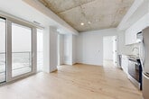 Located at 300 Miwate Pvt in Ottawa, this contemporary 2-bedroom, 2-bathroom unit offers a well-designed layout with refined industrial-modern finishes throughout. Exposed concrete ceilings contrast elegantly with crisp white walls and light-toned hardwood flooring, creating a clean, urban aesthetic that runs consistently through the space.

The open-concept living and kitchen area is bathed in natural light through expansive floor-to-ceiling windows and sliding glass doors that lead to a private balcony, offering panoramic views of the Ottawa River and surrounding cityscape. The kitchen features sleek white cabinetry reaching to the ceiling, stainless steel appliances including a refrigerator, range, microwave, and dishwasher, and a streamlined countertop workspace.

The primary bedroom is generously sized, with corner floor-to-ceiling windows and balcony access, maximizing both light and views. The second bedroom also benefits from large windows with balcony access. A connecting hallway links the two bedrooms to their respective bathrooms. The main bathroom includes a tub-shower combo with warm-toned tile, a white vanity, and large-format floor tiles. The ensuite features a walk-in shower with large-format wall tiles and a matching white vanity. Black hardware accents throughout add a contemporary finishing touch.