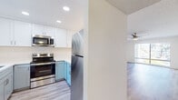 Located at 4302 Palm Ave in La Mesa, California, this single-floor residence offers a clean, updated interior with a cohesive modern design throughout. The open-concept living area is a standout feature, showcasing light wood-look flooring, crisp white walls, and a stylish gold-accented ceiling fan. A large sliding window floods the space with natural light and frames views of the surrounding greenery, enhancing the bright and airy ambiance.

The kitchen is thoughtfully designed with two-tone cabinetry — white upper cabinets paired with soft teal lower cabinets — complemented by white countertops and a full suite of stainless steel appliances, including an electric range, over-the-range microwave, and refrigerator. A breakfast bar with pendant lighting connects the kitchen to the living area.

The bedrooms feature plush neutral carpeting, ceiling fans, and windows with views of mature landscaping, including palm trees. Closet space is integrated into each room. The two bathrooms are finished in a contemporary style with white shaker-style cabinetry, white countertops, brushed hardware, and wood-look flooring. One bathroom offers a shower/tub combo, while the other features a sleek glass-enclosed walk-in shower. Textured ceilings are present throughout the space.