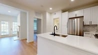 This thoughtfully designed 1-bedroom, 1-bathroom residence offers a clean, modern aesthetic throughout its efficiently utilized single-floor layout. The open-concept kitchen and living area serves as the heart of the home, anchored by a white kitchen island with a sleek quartz countertop and black matte pull-down faucet. The kitchen is fully equipped with stainless steel appliances—including a French door refrigerator, range, and built-in microwave—complemented by crisp white shaker cabinetry with black hardware and a herringbone tile backsplash. Light hardwood flooring flows seamlessly through the living areas and bedroom, creating a warm and cohesive atmosphere. The living room features a classic white-mantled fireplace flanked by natural light from windows with horizontal blinds. The bathroom is a standout, offering dual-sink white vanity cabinetry with black hardware, large-format neutral floor tile, and a marble-tiled tub and shower enclosure with gold-accented glass doors. The bedroom provides a comfortable, airy retreat, while the walk-in closet includes wire shelving for organized storage. A dedicated laundry room houses a full-size front-loading washer and dryer with overhead shelving, adding everyday convenience to this polished residence.
