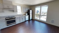 Located in the West Seattle neighborhood, Unit 401 at 4505 42nd Ave SW is a fourth-floor residence that combines modern design with functional living. Rich, dark hardwood flooring flows throughout the main living areas, creating a warm and cohesive aesthetic.

The open-concept kitchen is a standout feature, equipped with a full suite of stainless steel appliances including a refrigerator, range, dishwasher, and microwave. Gray shaker-style cabinetry with granite countertops provides ample storage and prep space, while a window above the sink allows natural light to filter in. Large windows in the adjacent living area frame elevated views of the surrounding Seattle cityscape and greenery, filling the space with abundant daylight.

The bedroom offers plush carpeting for comfort, a walk-in closet with built-in shelving, and a window with views of the neighborhood. A separate room with clean white walls and hardwood flooring provides flexible use as an office or additional living space.

The bathroom is thoughtfully designed with accessibility in mind, featuring grab bars, a wall-mounted vanity, and hardwood flooring that matches the rest of the unit. The overall palette throughout is clean and neutral, offering a bright, move-in-ready environment well-suited for comfortable urban living in Seattle.