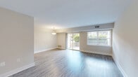 Located at 3602 Derwood Ln in Alexandria, Virginia, this single-floor, two-bedroom, one-bathroom home offers a practical and well-appointed layout. The spacious living room serves as the heart of the home, featuring rich hardwood-style flooring, neutral-toned walls, and abundant natural light streaming through a large sliding glass door and an adjacent picture window — both offering views of the outdoor greenery and providing direct access to a private patio. A pendant light fixture adds a refined touch to the open space. The kitchen is thoughtfully designed with modern flat-front cabinetry in a warm taupe finish, granite-style countertops, a white subway tile backsplash, and black appliances including a gas range, dishwasher, and refrigerator. The primary bedroom is generously sized, complete with plush carpeting, a closet with double doors, and a window for natural light. The second bedroom also features soft carpeting and a bright window with outdoor views. Both bedrooms offer a quiet, comfortable feel. The full bathroom includes a tiled tub-shower combination and clean, white fixtures. Three closets throughout provide ample storage. The home's cohesive neutral palette and mix of hardwood-style and carpeted floors create a clean, move-in-ready atmosphere.