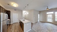 This 1-bedroom, 1-bathroom residence in Columbia, SC offers a thoughtfully designed open-concept layout that maximizes its comfortable footprint. The kitchen and living area flow seamlessly together, anchored by a central island with a granite countertop, undermount sink, and elegant pendant lighting. Dark espresso cabinetry extends to the ceiling, providing generous storage, while stainless steel appliances — including a refrigerator, range, and built-in microwave — add a polished, modern touch. A mosaic tile backsplash completes the kitchen's contemporary aesthetic. Wood-style flooring runs through the kitchen and transitions to plush carpet in the living and bedroom areas, adding warmth underfoot. The living room benefits from a ceiling fan and access to a private outdoor area through a glass door flanked by windows, allowing for natural light and outdoor views. The bedroom is a well-proportioned retreat featuring carpet flooring, a ceiling fan, multiple windows with blinds, and a closet. The bathroom includes a tiled tub-shower combination, a dark-cabinetry vanity with granite countertop, and tile flooring. A dedicated laundry area rounds out the functional layout of this move-in-ready residence.