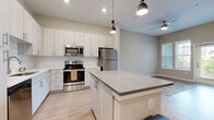 Located at 2035 Tapestry Park Drive in Indian Land, SC, this well-appointed one-bedroom, one-bathroom residence offers a thoughtfully designed open-concept layout with modern finishes throughout. The combined kitchen and living area serves as the heart of the home, featuring light wood-style flooring, soaring ceilings, and abundant natural light streaming in through large windows and a glass-panel exterior door. The kitchen is outfitted with crisp white shaker-style cabinetry, a classic subway tile backsplash, quartz countertops, a central island with pendant lighting, and a full suite of stainless steel appliances including a range, microwave, dishwasher, and refrigerator. The living area provides an open and airy feel with high ceilings and direct outdoor access. The bedroom is generously sized with plush carpeting, elevated ceilings, and windows that bring in natural light. It connects to a walk-in closet with built-in wire shelving for ample storage. The bathroom features light wood-tone cabinetry, a wide quartz-topped vanity, a large mirror, and wood-look flooring, creating a clean and contemporary feel throughout. The neutral color palette and modern design elements give the entire space a cohesive, move-in-ready aesthetic.