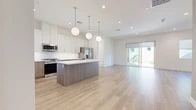 Located at 47320 Iris Way in La Quinta, California, this two-story home showcases a clean, contemporary design defined by bright white walls, light wood-tone flooring, and an open, airy layout. The main level centers around a well-appointed kitchen that flows seamlessly into the living area. The kitchen features white upper cabinetry, warm wood-toned lower cabinets and a matching center island with a white quartz countertop, stainless steel appliances including a gas range, built-in microwave, and french door refrigerator, and three globe pendant lights overhead. Sliding glass doors connect the living space to an outdoor area, filling the room with natural light. A dedicated laundry room on this level includes a full-size washer and dryer with overhead cabinetry and tile flooring.

The second floor offers additional living space with hardwood-style flooring, recessed lighting, and a ceiling fan. A sliding glass door opens to a private balcony with open views of the surrounding area. Bedrooms are carpeted and include generous closets, with one featuring a spacious walk-in closet with dual hanging rods and a high window. A full bathroom includes a glass-enclosed walk-in shower, wood-toned vanity, white quartz countertop, and large-format tile flooring.