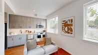 Located at 6400 America Blvd in Hyattsville, MD, this well-designed one-bedroom, one-bathroom unit makes smart use of its compact footprint across a single floor. The open-plan kitchen and living area form the heart of the space, anchored by warm hardwood flooring and bright white walls that create a clean, modern aesthetic. The kitchen features contemporary two-tone cabinetry — with upper wood-grain panels and lower gray base cabinets — complemented by white subway tile backsplash, light countertops, and stainless steel appliances including a range, microwave, and dishwasher. Large windows throughout the unit invite abundant natural light and offer views of lush greenery outside. The living area provides a comfortable, open setting adjacent to the kitchen. A light-filled hallway lined with louvered closet doors connects the main living space to the private bedroom, which offers two sets of double closets for generous storage. The bedroom is a cozy retreat with warm hardwood floors and windows that add brightness. The full bathroom is finished with marble-look tile flooring, white subway tile surrounding a soaking tub/shower combination, and clean white fixtures. With four closets distributed throughout, this unit delivers practical, well-organized living in a contemporary package.