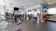 Located at 201 S 25th Street in Philadelphia, PA, this well-appointed fitness center offers a comprehensive workout environment designed to accommodate a wide range of training needs. The open, single-floor layout provides ample space for movement and exercise, creating an inviting atmosphere for both casual gym-goers and dedicated athletes.

The strength training area is extensively equipped, featuring a full dumbbell rack with a broad selection of weights, multiple weight benches, barbells with plate storage, and a cable machine system for versatile resistance training. Exercise balls in various sizes are neatly organized along the perimeter, offering options for functional and core-focused workouts.

The space is finished with durable rubber flooring, ideal for heavy equipment and high-intensity training. Large mirrors line the walls, enhancing the sense of openness while allowing users to monitor their form. Recessed lighting and circular pendant fixtures provide bright, even illumination throughout the floor, complemented by natural light from nearby windows.

Overhead, a mounted flat-screen television adds an entertainment element to the training environment. The clean white walls, drop-panel ceiling, and modern design details give the facility a polished, professional aesthetic that reflects a commitment to a quality fitness experience.