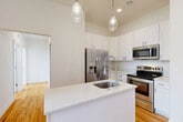 Located at 550 N Holbrook St in Plymouth, MI, this well-appointed 2-bedroom unit offers a thoughtfully designed single-floor layout that maximizes both comfort and functionality. The kitchen serves as a centerpiece of the home, boasting soaring ceilings, crisp white shaker cabinetry, a quartz-topped island with an undermount sink and pendant lighting, and a full suite of stainless steel appliances including a French door refrigerator, electric range, and built-in microwave. Warm hardwood flooring extends throughout the living areas and bedrooms, creating a cohesive and inviting atmosphere. The living room flows naturally from the kitchen, offering an open and airy feel enhanced by the impressive ceiling height. The primary bedroom provides a comfortable retreat, while the second bedroom features large multi-pane windows that fill the room with natural light and offer pleasant views of the surrounding neighborhood. Three closets offer generous storage throughout the unit. The bathroom is finished with elegant marble-look tile flooring and a full tub-shower surround, lending a clean, upscale aesthetic. Additional conveniences include a dedicated laundry area and a utility room, rounding out this efficient and modern space.
