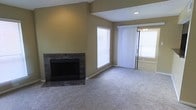 This single-floor residence offers a welcoming and functional layout designed for comfortable everyday living. The living area serves as the heart of the home, anchored by a striking fireplace with a dark granite surround that adds a refined focal point to the room. Plush wall-to-wall carpeting runs throughout, contributing to a warm and inviting atmosphere underfoot. Natural light fills the space generously through a large window fitted with horizontal blinds, as well as a sliding glass door dressed with vertical blinds that provides access to the outdoors. Vaulted or angled ceiling details lend a sense of added height and architectural interest to the living area, enhancing the overall sense of openness. Recessed lighting complements the natural illumination, ensuring the space remains well-lit at all hours. The warm neutral tones of the walls tie the room together cohesively, creating a calm and understated palette that suits a variety of décor styles. Overall, this residence presents a clean, move-in ready environment with practical features and timeless design elements throughout.
