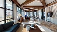 Located on Maybank Highway in Charleston, South Carolina, this single-story community clubhouse delivers a refined, coastal-inspired atmosphere through a thoughtful blend of architectural detail and modern design. Prominent exposed wood beams traverse the vaulted ceilings throughout the space, lending warmth and a distinctly Southern character to the interior. Underfoot, chevron-patterned hardwood flooring adds visual depth and a sophisticated rhythm that carries consistently across the main areas.

Expansive floor-to-ceiling windows with black steel frames flood the interior with abundant natural light while offering open views of the surrounding outdoor amenity spaces, including palm-lined courtyards and resort-style pool areas. The lounge area features a comfortable seating arrangement anchored by a deep teal sofa, a wall-mounted television, and curated coastal décor.

The central area transitions into a leasing and workspace zone, where multiple workstations and seating arrangements support both staff and resident needs. A dedicated refreshment station with cabinetry, a beverage cooler, and a textured geometric accent wall serves as a functional and stylish focal point. Pendant and chandelier lighting complements the natural light throughout, creating a welcoming and well-appointed environment overall.