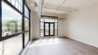 Located in the heart of Dayton, Ohio, this three-bedroom, two-bathroom loft-style residence offers a compelling blend of industrial character and modern comfort across a single floor. The open living area immediately impresses with large black-framed floor-to-ceiling windows and French doors that flood the space with natural light while offering views of the surrounding cityscape. Exposed silver ductwork and brass piping run overhead, lending an authentic industrial aesthetic that defines the space's personality.

The kitchen and dining area are well-appointed, featuring warm honey-toned cabinetry, granite-style countertops, and a full suite of black appliances including a refrigerator, electric range with overhead microwave, and dishwasher. Light hardwood-style flooring runs throughout, tying the open-concept layout together seamlessly.

Three generously sized bedrooms offer clean, neutral interiors with continued exposed ductwork details and structural beam accents. One bedroom features a closet with louvered bi-fold doors and wire shelving, alongside a window with urban views. The hallways are bright and well-proportioned, connecting the rooms efficiently.

Both bathrooms are finished with dark-toned vanities, white countertops, mirrored medicine cabinets, and hardwood-style flooring. The layout is practical and cohesive throughout, making this an excellent urban residence in downtown Dayton.
