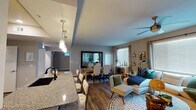 This single-floor residence is designed around an open-concept layout that seamlessly connects the kitchen, dining, and living areas, creating a spacious and cohesive environment. The kitchen is outfitted with dark espresso cabinetry, granite countertops, stainless steel appliances including a gas range with a bold overhead hood, and a decorative tile backsplash. A large island with seating extends the kitchen into the main living space, with pendant lighting overhead adding a polished touch.

The dining area accommodates a full-sized table with upholstered chairs and features a large wall mirror that enhances the sense of depth, alongside windows that invite natural light. Adjacent to it, the living room is warm and inviting, highlighted by a ceiling fan, large windows with blinds, and hardwood-style flooring throughout the main areas.

The bedrooms are carpeted and generously sized, each equipped with ceiling fans and windows providing natural light; one bedroom features a trio of clerestory windows alongside a standard window for added brightness. The bathroom includes a combination tub and shower, dark-finished fixtures, a granite-topped vanity with dark cabinetry, and wood-style flooring.