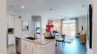 This 2-bedroom, 2-bathroom residence delivers a modern, open-concept layout designed for comfortable everyday living. The kitchen serves as the heart of the home, featuring crisp white cabinetry, granite countertops, a tile backsplash, stainless steel appliances — including a range, microwave, and refrigerator — and a large island with bar seating, ideal for casual dining or entertaining. Light wood-style flooring flows seamlessly from the kitchen into the combined dining and living area, where large sliding glass doors and windows flood the space with natural light and provide direct access to a private balcony with outdoor views. The living room offers a bright, airy ambiance accentuated by a ceiling fan and recessed lighting. The spacious primary bedroom includes plush carpeting, a ceiling fan, large windows, and a dedicated en-suite bathroom. A well-organized walk-in closet with built-in wire shelving and storage bins provides generous storage. The second bedroom is equally comfortable, featuring a ceiling fan and ample natural light. Both bathrooms are thoughtfully finished. Throughout the residence, clean lines, neutral tones, and contemporary finishes create a cohesive and inviting atmosphere.