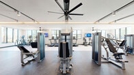 Located at 495 Centerpointe Circle in Altamonte Springs, Florida, this generously sized fitness center offers a comprehensive and modern workout environment spread across a single, open floor. The facility is designed with a clean, contemporary aesthetic, featuring coffered ceilings with integrated LED accent lighting, large ceiling fans for airflow, and an abundance of natural light streaming through oversized windows that frame views of the surrounding outdoor greenery and skyline.

The gym is thoughtfully zoned to accommodate a wide range of fitness activities. A dedicated cardio area houses a row of treadmills, recumbent bikes, upright cycles, and elliptical machines — many positioned to take advantage of the natural light and exterior views. Wall-mounted flat-screen televisions are positioned throughout for entertainment during workouts.

The strength training section features an extensive lineup of Matrix-brand cable and resistance machines alongside free-weight and bench press stations. Full-length mirrors line key walls, enhancing the sense of space and supporting proper form during exercise. A separate functional training area with a smooth hardwood-style floor provides space for stretching, cycling classes, and group workouts. The flooring transitions seamlessly between rubberized gym surfaces and light wood-toned areas, reflecting the facility's dual-purpose design. Overall, the space delivers a polished, high-end fitness experience.