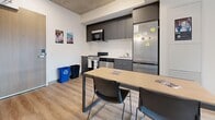 This 360 square foot apartment in Hamilton, Ontario offers a well-designed living space with two bedrooms and one bathroom. The layout efficiently utilizes every inch of the compact floor plan. The primary bedroom, measuring 100 square feet, features built-in storage and a large window offering city views.

The kitchen boasts modern gray cabinetry, stainless steel appliances, and a sleek white backsplash. A dining area adjacent to the kitchen provides space for meals and studying. The bathroom includes a white shower stall with built-in shelving for convenience.

Throughout the apartment, wood-look flooring adds warmth and durability. Large windows in the living areas and bedrooms allow ample natural light and showcase urban vistas. The living room accommodates a sofa and offers flexibility for various layouts.

Despite its small footprint, the apartment incorporates smart storage solutions and a contemporary aesthetic. The concrete ceiling adds an industrial touch, while white walls keep the space feeling open and bright. This efficient urban dwelling is well-suited for students or young professionals seeking a stylish, low-maintenance living space in downtown Hamilton.