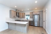Located at 6328 W State St in Boise, Idaho, this contemporary three-story home showcases modern design with clean lines and quality finishes throughout. The interior is characterized by crisp white walls, light-toned luxury vinyl plank flooring on the main level, and plush carpeting in the upper-floor rooms, creating a cohesive and inviting aesthetic.

The kitchen serves as a central highlight, featuring light wood cabinetry with matte black hardware, white quartz countertops, a subway tile backsplash, and a full suite of stainless steel appliances including a gas range, dishwasher, and French door refrigerator. A wall-mounted range hood and a central island with seating add both function and style.

The bathrooms are tastefully finished with light wood vanities, white quartz surfaces, stone tile flooring, and matte black fixtures. The primary bathroom includes a dual-sink vanity, a sliding barn door, and an adjacent walk-in closet, while a secondary bath offers a tiled tub-shower combination.

Carpeted bedrooms provide natural light through well-placed windows. A dedicated laundry room with a full-size Whirlpool washer and dryer adds everyday convenience. Carpeted stairs connect all three floors of this thoughtfully designed Boise home.