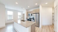 This two-story residence offers a well-organized layout across two floors, with the main living areas situated on the upper level. The open-concept kitchen and living room serve as the heart of the home, featuring light hardwood-style flooring, recessed lighting, and an abundance of natural light from multiple windows. The kitchen is outfitted with stainless steel appliances, including a refrigerator, electric range, and microwave, complemented by taupe shaker-style cabinetry and a central island with a granite countertop and undermount sink — ideal for both meal preparation and casual dining.

Both bedrooms are generously proportioned, with the primary bedroom offering notable space. Each bedroom features soft carpeting, ceiling fans, and windows that provide views of the surrounding area. Dedicated closets serve each bedroom, adding practical storage throughout.

The two bathrooms are cleanly finished, with one featuring a full tub and shower combination adorned with white square tile surround and chrome fixtures. A carpeted staircase with a handrail connects the entry level to the main floor, adding a soft, welcoming transition between levels. The overall aesthetic is bright and contemporary, with a neutral color palette creating a clean and inviting atmosphere throughout.