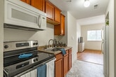 This one-bedroom, one-bathroom unit at Kings Reserve offers a well-organized, single-floor layout that maximizes every square foot of its compact footprint. The kitchen is outfitted with warm wood cabinetry, granite-look countertops, a stainless steel sink, an electric range, and an overhead microwave, with light tile flooring and a clean, efficient design throughout.

The living room features warm hardwood-style flooring, neutral cream walls, and a large window fitted with blinds that allows natural light to filter in while offering views of surrounding greenery. Wall sconces provide ambient lighting, complementing the bright and airy atmosphere.

The bedroom continues the hardwood-style flooring and neutral palette, with a wide window offering pleasant outdoor views of tree canopy. Wall sconces flank the sleeping area, and a closet provides storage. The room is cozy yet functional.

The bathroom is elongated and well-proportioned, featuring tile flooring, a vanity with matching wood cabinetry and granite-look countertop, and a walk-in shower with grab bars — a practical and accessibility-conscious design. Overall, the unit presents a clean, light-filled living environment suitable for efficient, comfortable daily living.