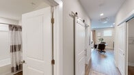 Located in Huntsville, Alabama, this single-floor residence at Dallas St NE offers a thoughtfully designed layout with modern finishes throughout. Light-toned hardwood-style flooring flows continuously across the main living areas, complementing the neutral warm-gray wall palette that lends a cohesive, contemporary feel to the space.

The kitchen is well-appointed with rich dark-toned cabinetry providing ample storage, light countertops, and a full suite of stainless steel appliances including a range, microwave, dishwasher, and refrigerator. A window above the counter allows natural light to brighten the space. The adjoining dining area accommodates a dining table, creating a seamless kitchen-to-dining transition.

The living area features interior transom-style windows that borrow light between rooms, along with recessed lighting and access to the hallway. A stylish sliding barn door with polished chrome hardware adds a modern-industrial design element to the corridor, which connects the main living spaces to the private areas.

The bedroom offers a comfortable, well-scaled layout with carpeted flooring, recessed ceiling features, and a transom window detail. The full bathroom includes a vanity with wood-toned cabinetry, a tub-shower combination, and clean, light finishes throughout, maintaining the unit's consistent modern aesthetic.