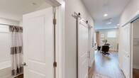 Located in Huntsville, Alabama, this single-floor residence at Dallas St NE offers a thoughtfully designed layout with modern finishes throughout. Light-toned hardwood-style flooring flows continuously across the main living areas, complementing the neutral warm-gray wall palette that lends a cohesive, contemporary feel to the space.

The kitchen is well-appointed with rich dark-toned cabinetry providing ample storage, light countertops, and a full suite of stainless steel appliances including a range, microwave, dishwasher, and refrigerator. A window above the counter allows natural light to brighten the space. The adjoining dining area accommodates a dining table, creating a seamless kitchen-to-dining transition.

The living area features interior transom-style windows that borrow light between rooms, along with recessed lighting and access to the hallway. A stylish sliding barn door with polished chrome hardware adds a modern-industrial design element to the corridor, which connects the main living spaces to the private areas.

The bedroom offers a comfortable, well-scaled layout with carpeted flooring, recessed ceiling features, and a transom window detail. The full bathroom includes a vanity with wood-toned cabinetry, a tub-shower combination, and clean, light finishes throughout, maintaining the unit's consistent modern aesthetic.