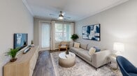 Located at 6880 Rivers Ave in North Charleston, SC, this one-bedroom, one-bathroom unit offers a thoughtfully designed single-floor layout that maximizes its comfortable footprint. The open-concept living and kitchen area forms the heart of the space, with wood-style flooring, crown molding, and neutral gray tones throughout creating a cohesive, modern aesthetic. The living room features a ceiling fan with light fixture, large windows with outdoor access that invite natural light, and ample room for furnishings.

The kitchen is well-equipped with dark espresso cabinetry extending to the ceiling for generous storage, light granite-style countertops, black appliances including a range, microwave, and refrigerator, and a sink. A dedicated closet adjacent to the kitchen houses a stacked washer and dryer unit, adding everyday convenience.

The carpeted bedroom is spacious, accommodating a large bed comfortably, and includes a ceiling fan, natural light from a window with blinds and curtains, and access to a closet. The bathroom features wood-look tile flooring, a dark vanity with a marble-style countertop, a full tub-shower combination, and clean white finishes throughout, completing this efficiently designed and attractively finished residence.