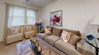 This two-floor residence offers a thoughtfully designed layout that balances comfort and functionality throughout its living spaces. The kitchen serves as a central highlight, featuring rich warm-toned wood cabinetry, light stone countertops, stainless steel appliances including a range, over-the-range microwave, and refrigerator, as well as a peninsula breakfast bar with seating — ideal for casual dining and entertaining. A skylight adds a bright, airy quality to the kitchen area. Durable wood-look flooring runs through the kitchen and entry areas, while plush carpeting provides comfort in the living room and bedrooms. The living room opens toward the front entry, which includes a transom window above the door, allowing natural light to filter in. A dedicated sitting area features large windows with views of surrounding greenery, creating a welcoming retreat. The generously sized primary bedroom accommodates a king-sized bed with ease, offering multiple windows and soft, neutral tones throughout. Two full bathrooms are finished with tile flooring, dark wood vanities, light stone countertops, and tub-shower combinations, maintaining a consistent and cohesive aesthetic. Overall, the space presents a warm, neutral palette with functional design details across every room.